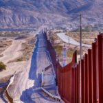 Controversy and Legal Challenges Surrounding Brian Kolfage’s Border Wall Initiative Border wall stretching through desert landscape with mountains.