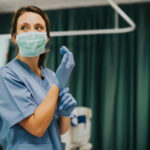 Hospital Executives ARRESTED — Killer NURSE Cover-Up Exposed… Nurse wearing scrubs and mask putting on gloves.