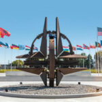 Pentagon LEAK Exposes NATO Suspension Plot…. NATO emblem with flags of member countries in background.
