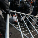 ARREST MADE: Bomb Plot Targets Conservative ICON…. Police in riot gear detain a person on the ground near a toppled metal barricade
