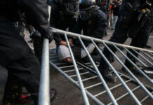 ARREST MADE: Bomb Plot Targets Conservative ICON…. Police in riot gear detain a person on the ground near a toppled metal barricade