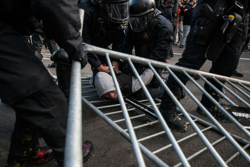 Police in riot gear detain a person on the ground near a toppled metal barricade