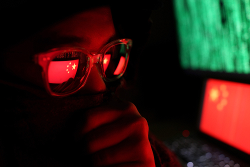 shutterstock_1339292228.jpg Person wearing glasses with a reflection of the Chinese flag, surrounded by computer screens