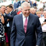 WATCH: Masked Attacker Targets Prince Andrew… A man in a suit smiling crowd in background.