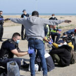 Police officers assist migrants on a beach.