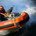 163 DEAD at Sea—Were They Really Narco-Terrorists? Person on orange boat holding machine gun.