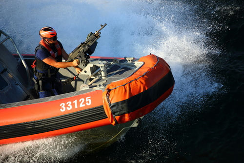 shutterstock_375381499.jpg Person on orange boat holding machine gun.