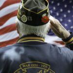 VETERAN Charged $21K for Own Benefits! Veteran saluting in front of American flag.