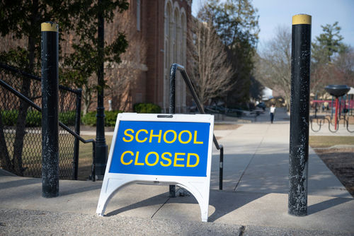 shutterstock_1688108254 School closed sign on sidewalk near building.