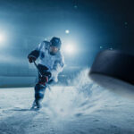 NHL SHOCKER: Star Suddenly Can’t Walk…. A hockey player shooting a puck on an ice rink under bright arena lights
