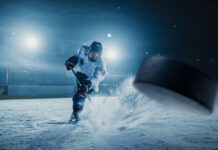 A hockey player shooting a puck on an ice rink under bright arena lights