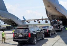 Military aircraft unloading vehicles at an airport with security personnel present