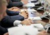 AI Spending Sucker-Punches IBM Business meeting participants with hands clasped at a conference table with microphones