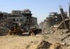 People walk through a street of destroyed buildings and rubble