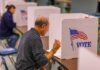 Man voting in a booth with American flag.