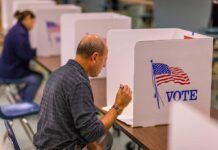 Man voting in a booth with American flag.