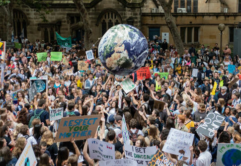 Crowd at climate protest holding signs and large Earth balloon.
