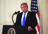 Donald Trump speaking at a podium with American flag.