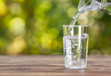 Pouring water into a glass on wooden table.