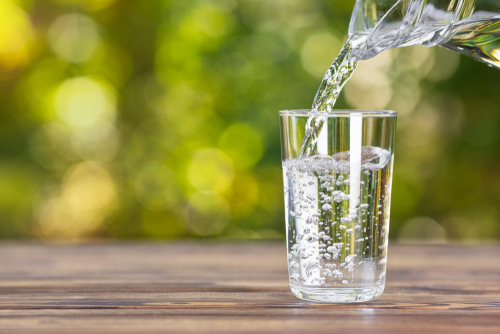 Pouring water into a glass on wooden table.