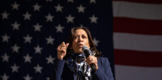 A person speaking in front of an American flag.