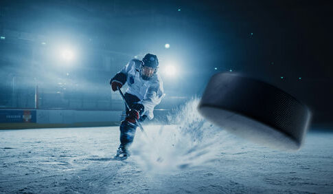 A hockey player shooting a puck on an ice rink under bright arena lights