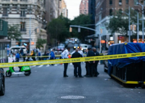 Police officers behind yellow crime scene tape on city street.