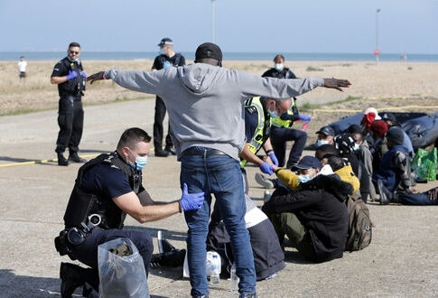 Police officers assist migrants on a beach.