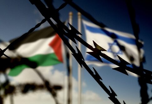 Barbed wire in the foreground with Palestinian and Israeli flags in the background
