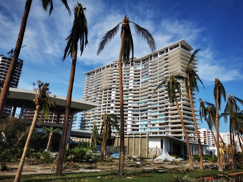 Damaged high-rise building with bent palm trees around.