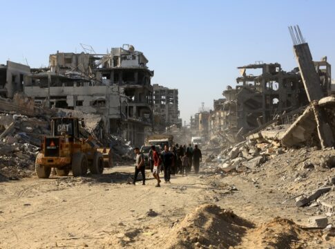 People walk through a street of destroyed buildings and rubble