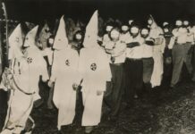 Ku Klux Klan members marching in white robes and hoods.