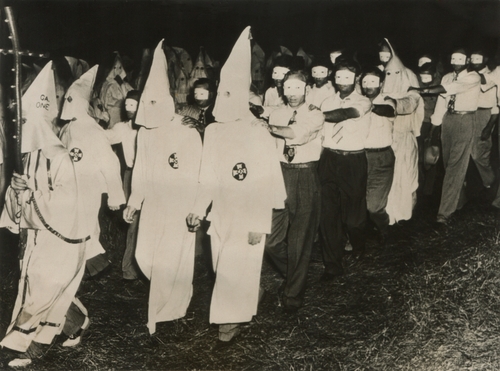 Ku Klux Klan members marching in white robes and hoods.