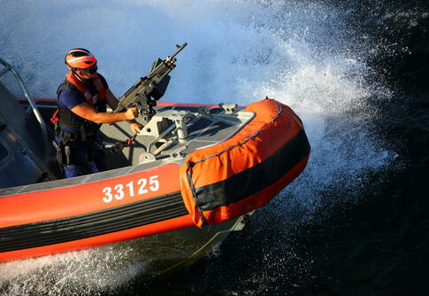 Person on orange boat holding machine gun.