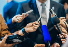 Multiple microphones held towards a person in suit.