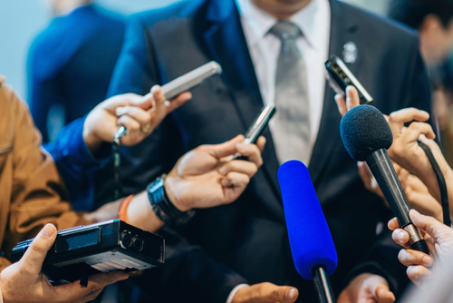 Multiple microphones held towards a person in suit.